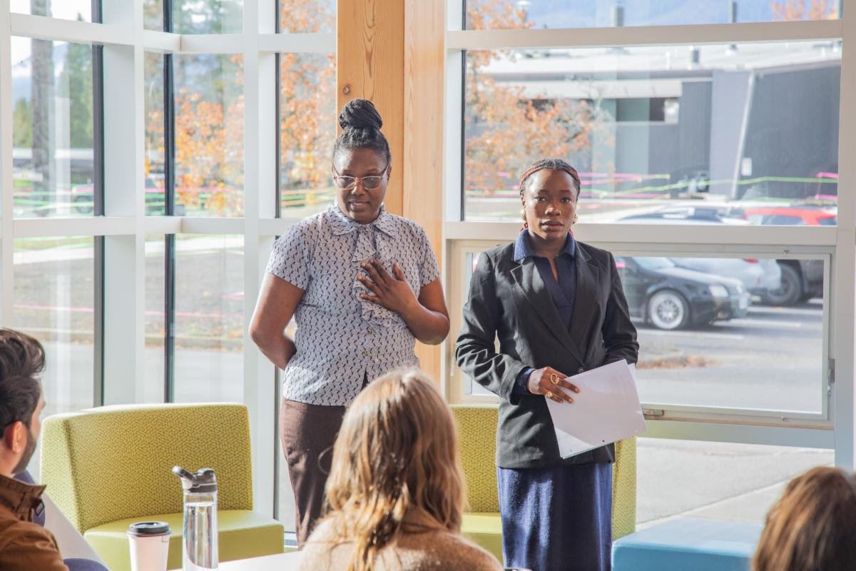 Two students presenting to a group in a bright campus atrium