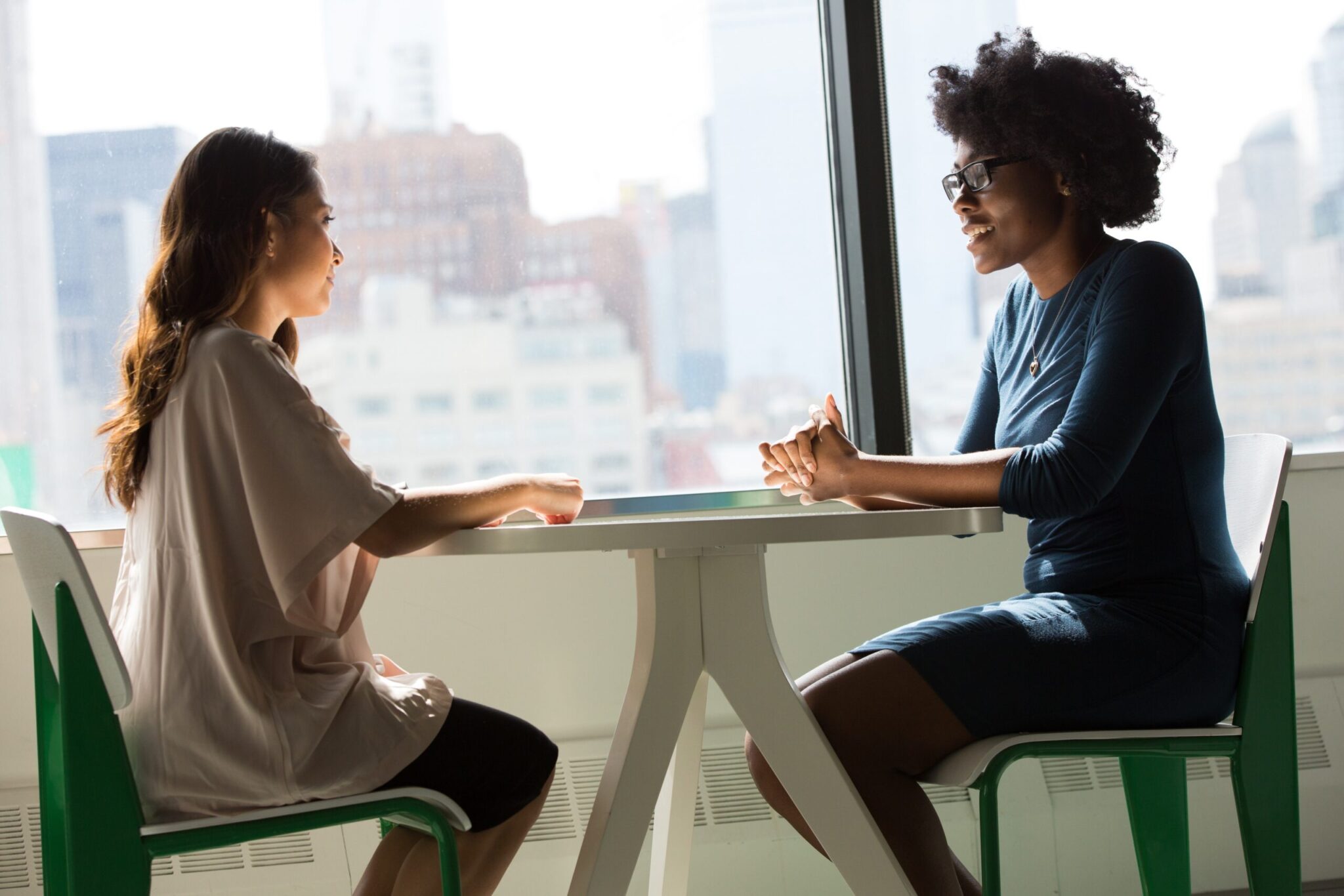 Two professionals in conversation across a table in a bright office