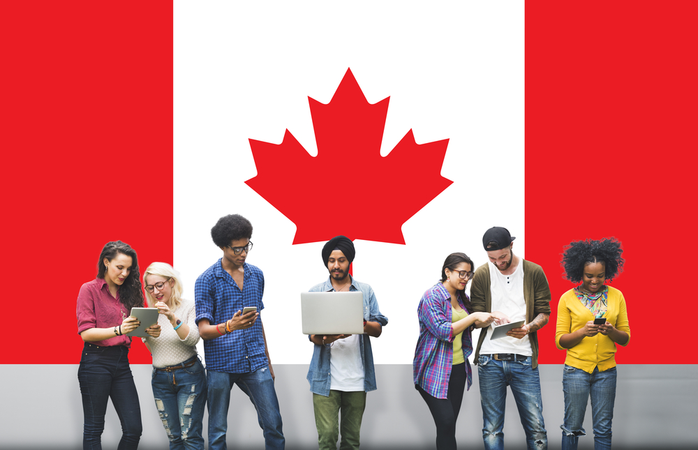 A group of international students standing in front of a large Canadian flag backdrop