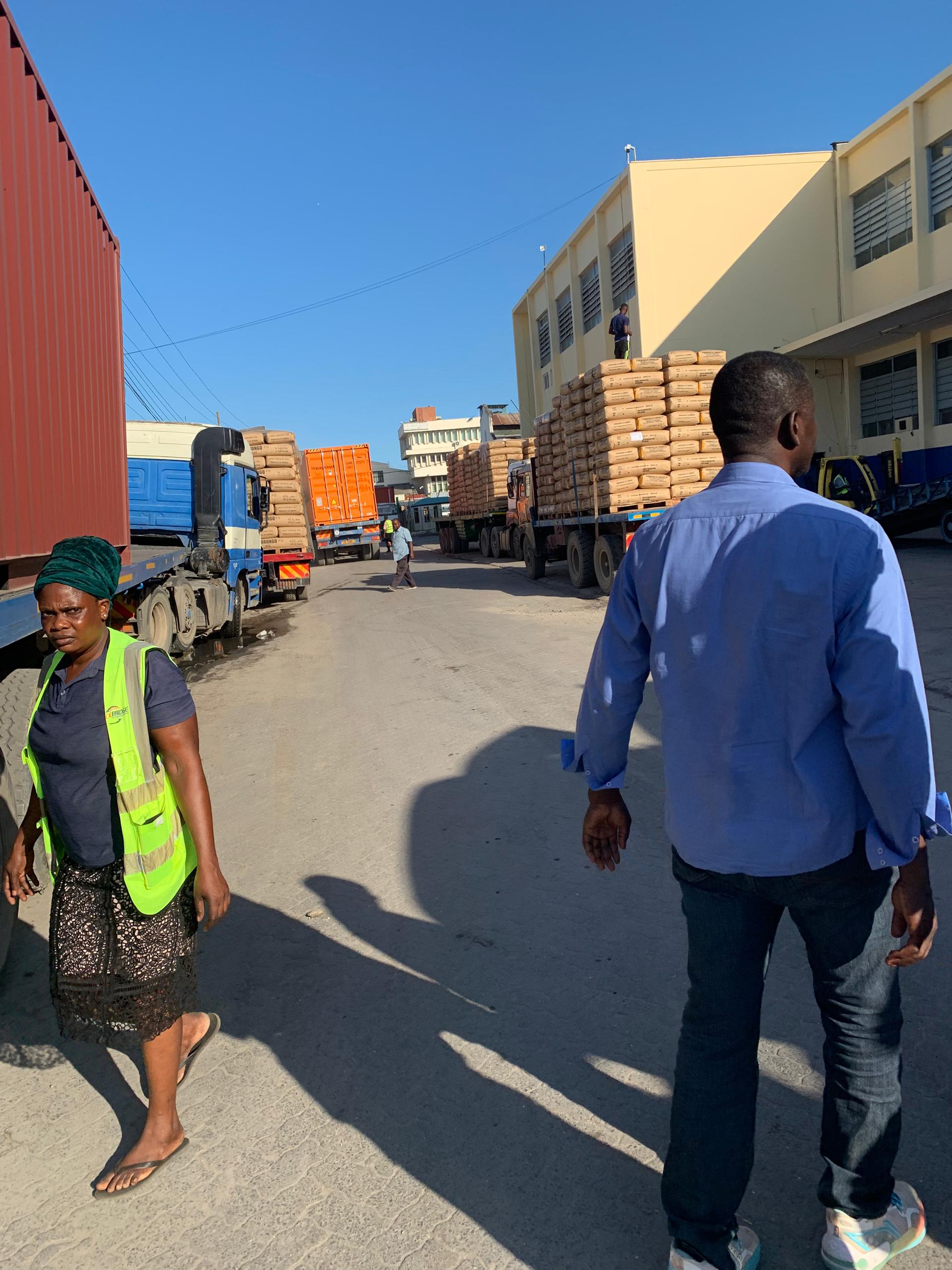 ACTC trucks loaded with bagged goods at a sunny loading yard, a worker in a hi-vis vest walking past