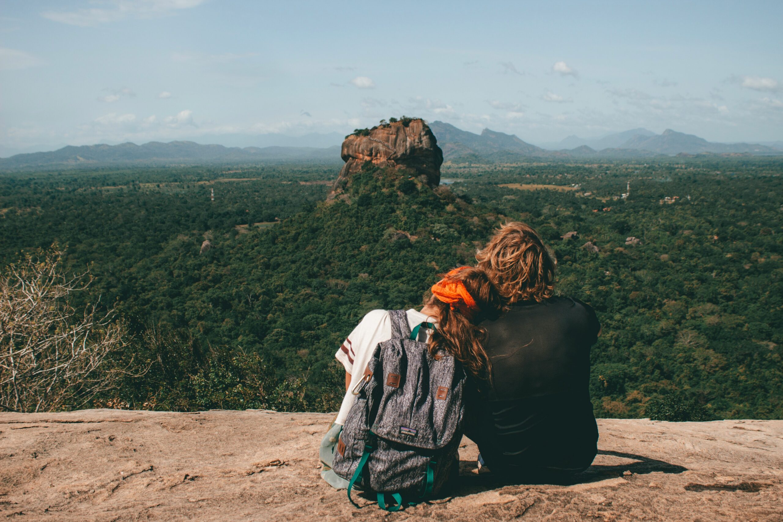 Two travellers resting on a rock ledge with Sigiriya, Sri Lanka's Lion Rock, rising from the forest behind them